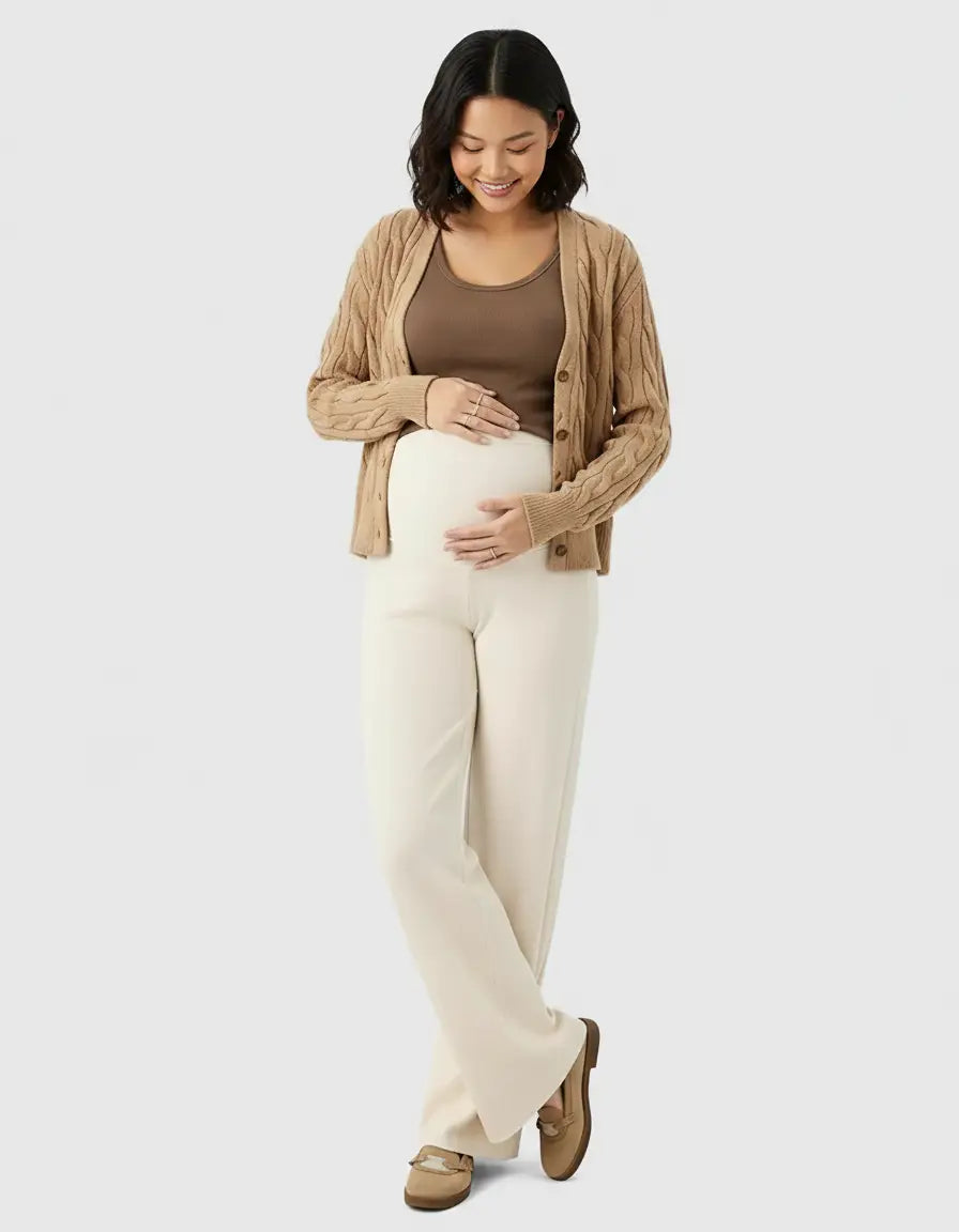 Pregnant woman in cream high-waist wide-leg wool pants, brown tank top, and cable-knit cardigan.