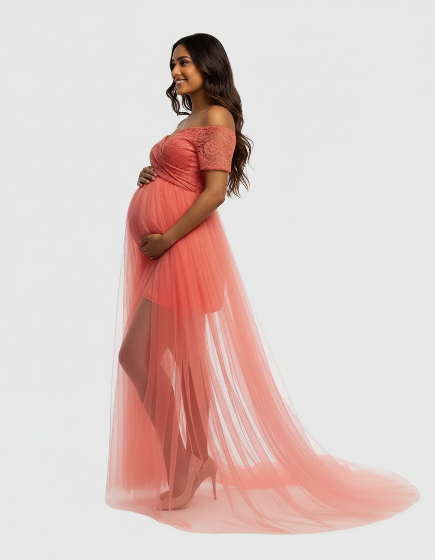 Smiling pregnant woman in a coral lace and mesh off-shoulder maternity gown with a flowing tulle skirt.