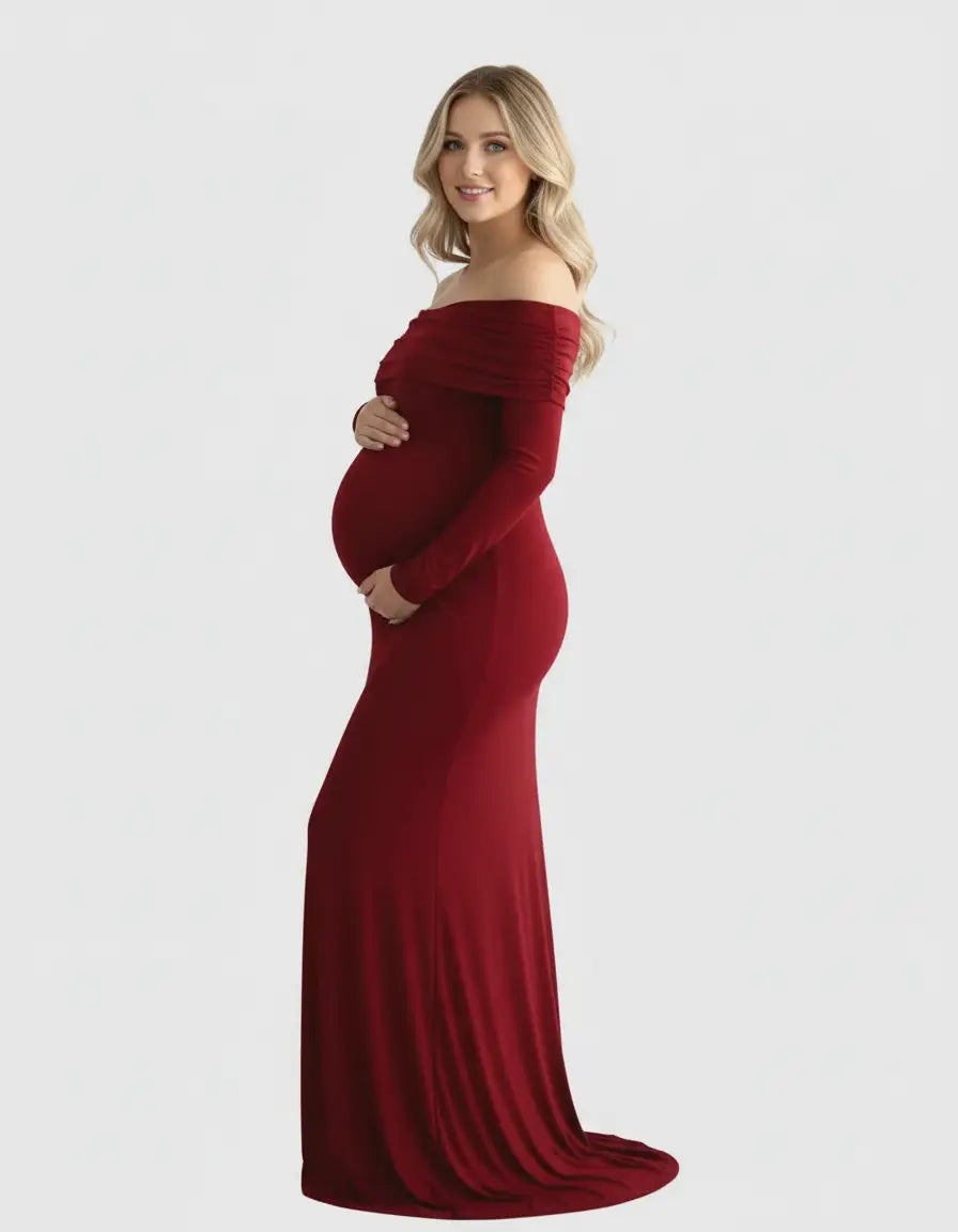 Blonde pregnant woman in a long, flowing, off-shoulder, cross-back, dark red maternity gown.