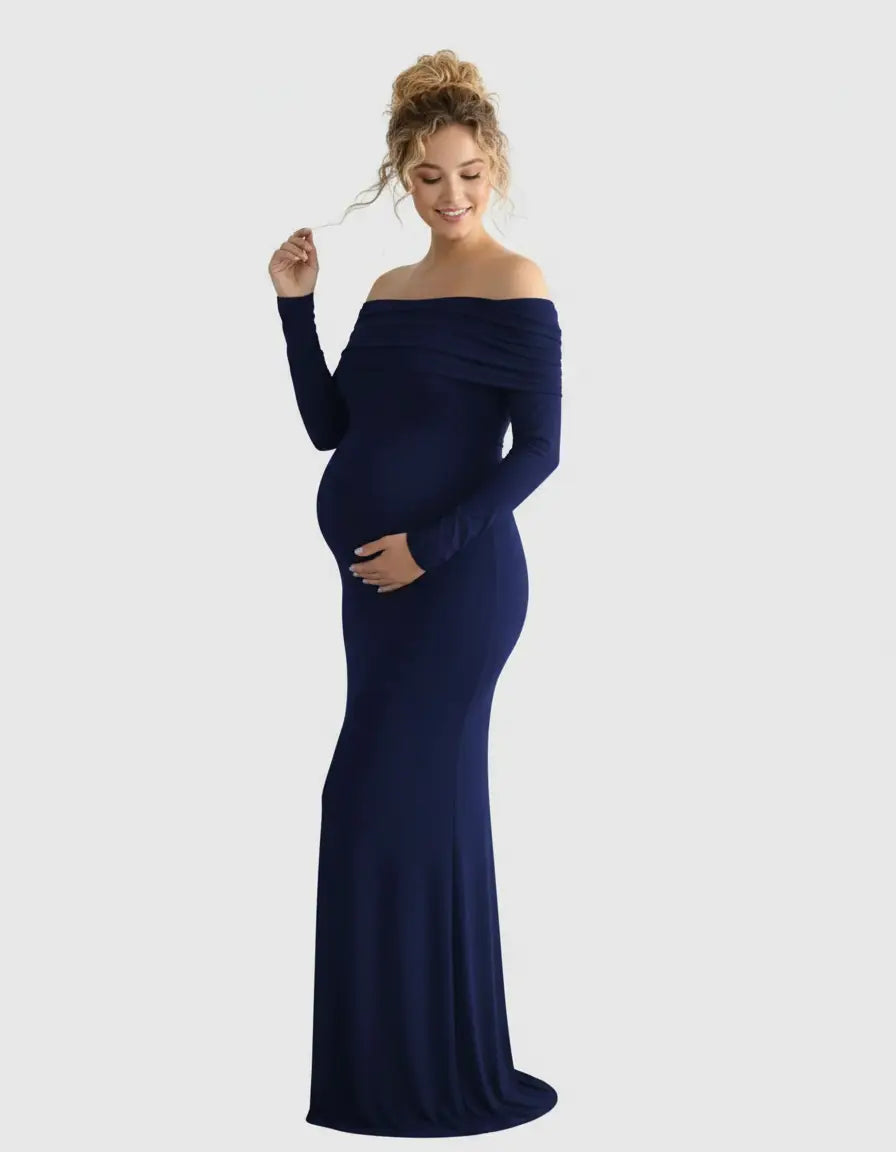Smiling pregnant woman in a navy off-shoulder, long-sleeve maternity gown, cradling her bump.