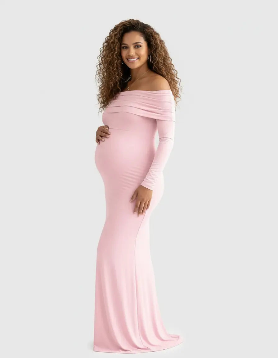 Smiling pregnant woman in a pink off-shoulder, long-sleeve, cross-back maternity gown.