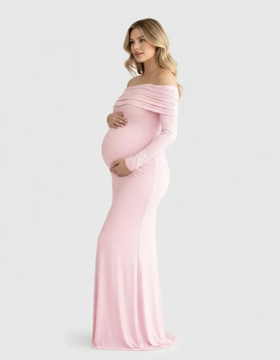 Blonde pregnant woman in a long, pink off-shoulder cross-back maternity gown.