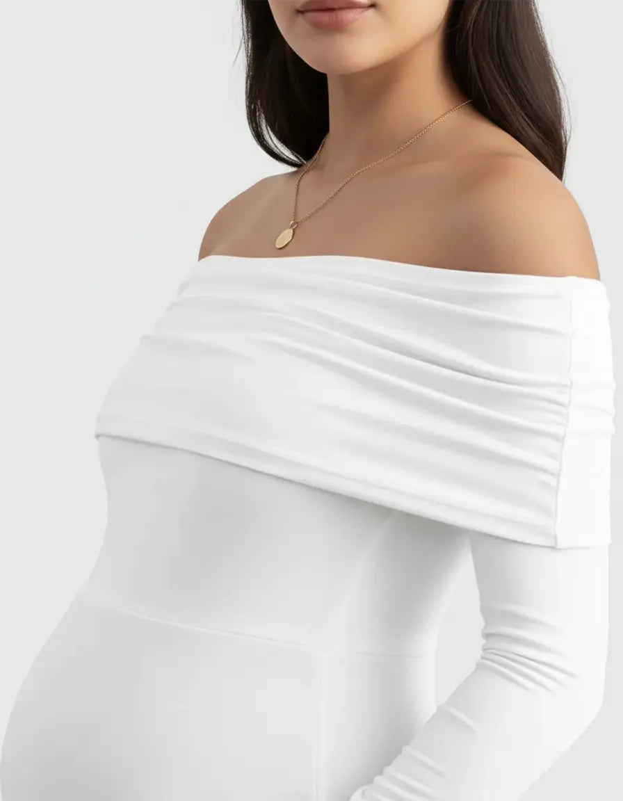 White off-shoulder cross-back maternity gown with long sleeves, soft ruched fabric, and a gold necklace.