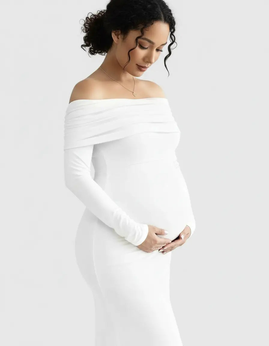 Pregnant woman in a white off-shoulder, long-sleeve maternity gown, gently cradling her belly.