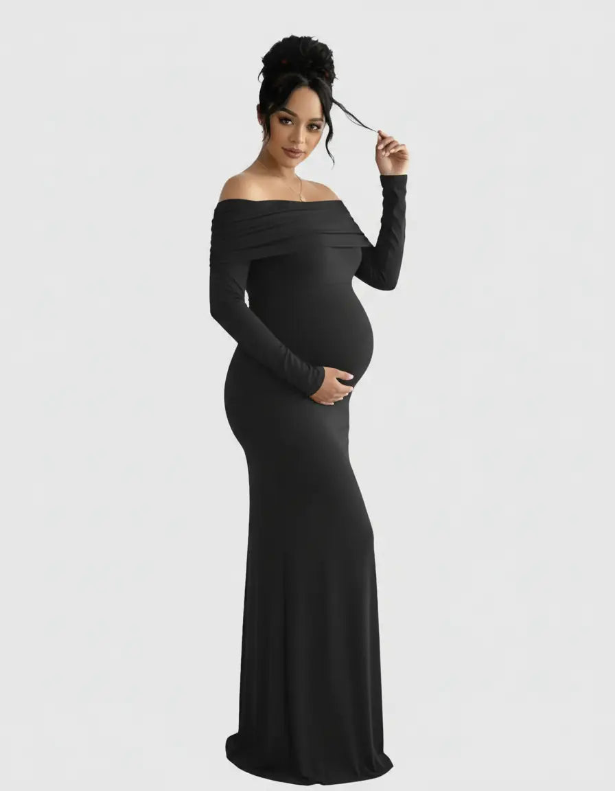 Pregnant woman in a black off-shoulder cross-back maternity gown, holding her baby bump.