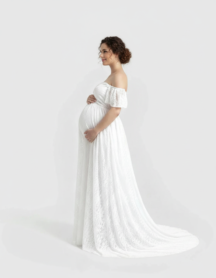 Pregnant woman in a white off-shoulder flowing lace maternity maxi dress, smiling.