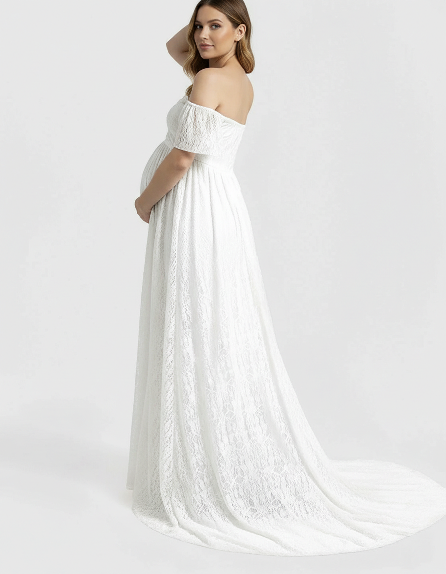 Pregnant woman in a white off-shoulder flowing lace maternity maxi dress, holding her bump.