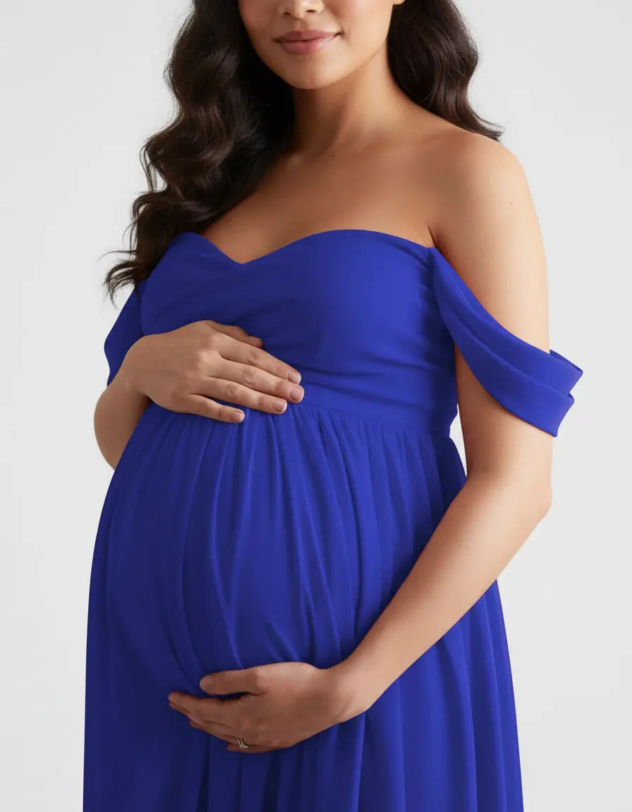 Pregnant woman in a flowing, royal blue off-shoulder maternity gown, hands cradling her bump.