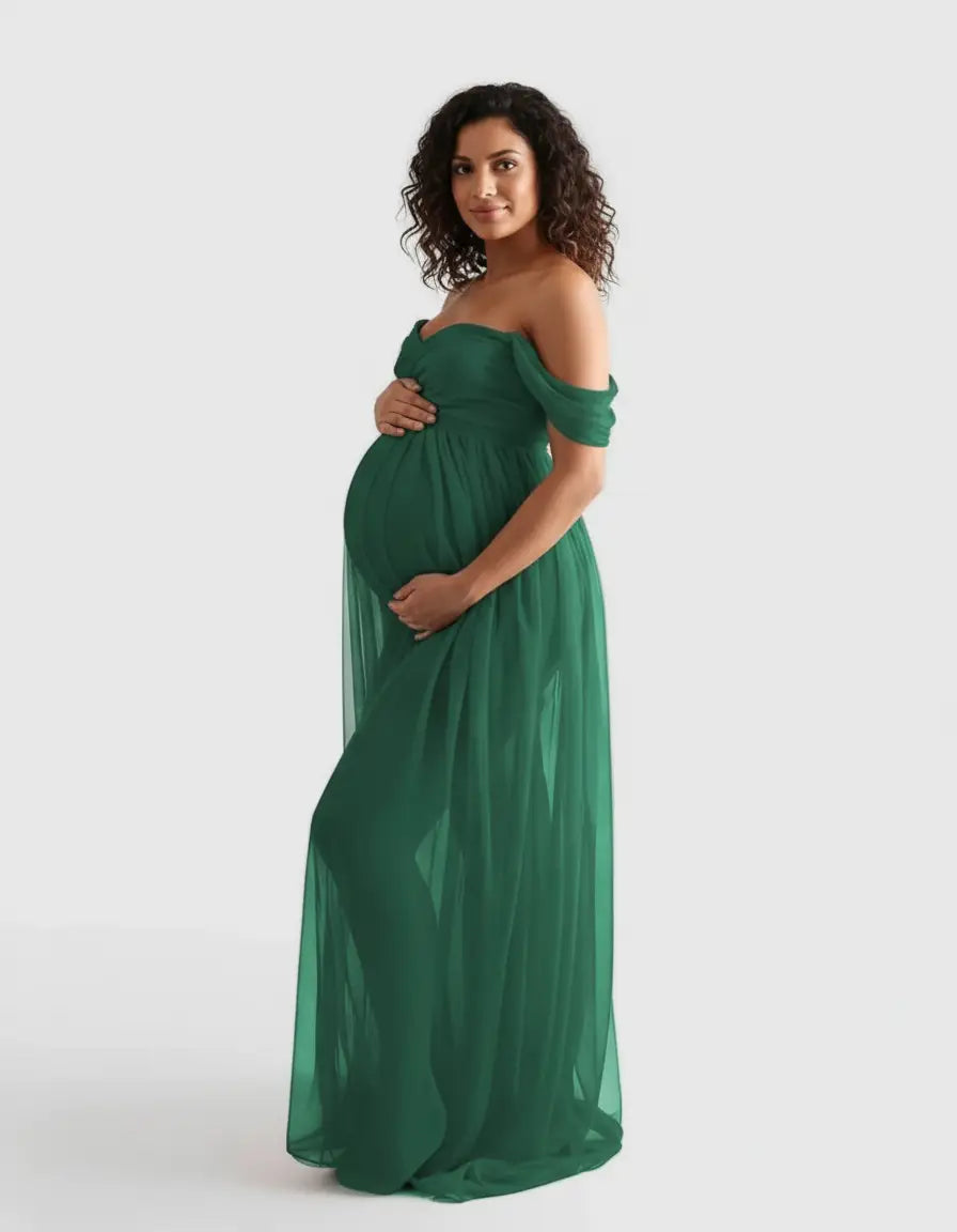 Smiling pregnant woman in a flowing, off-shoulder emerald green maternity photoshoot gown.