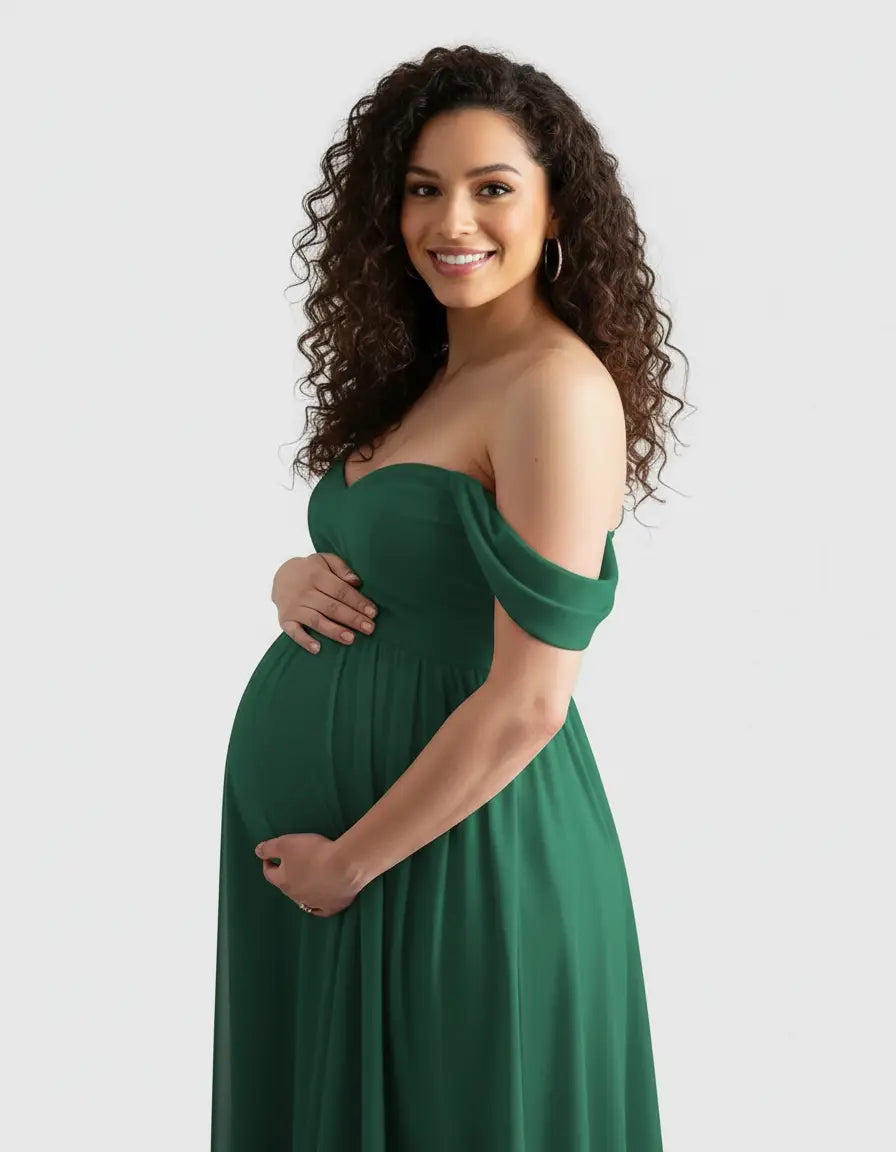 Smiling pregnant woman in a flowing, off-shoulder emerald green maternity photoshoot gown.