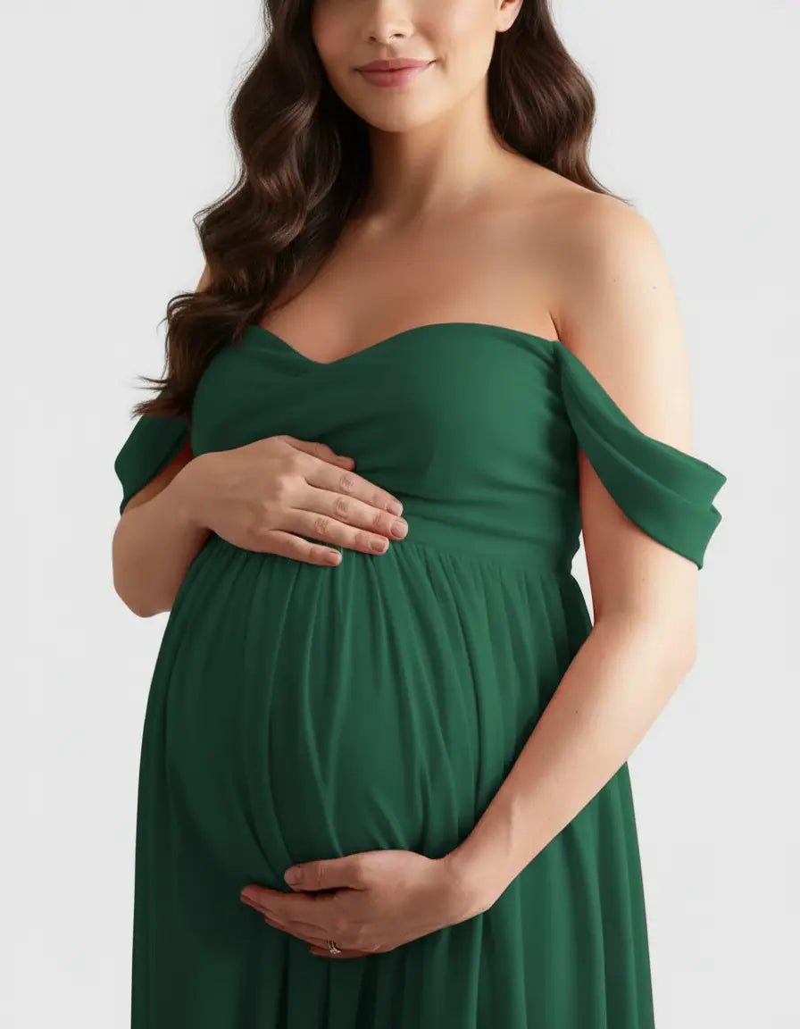 Maternity model in a flowing, off-shoulder emerald green gown, cradling her baby bump.