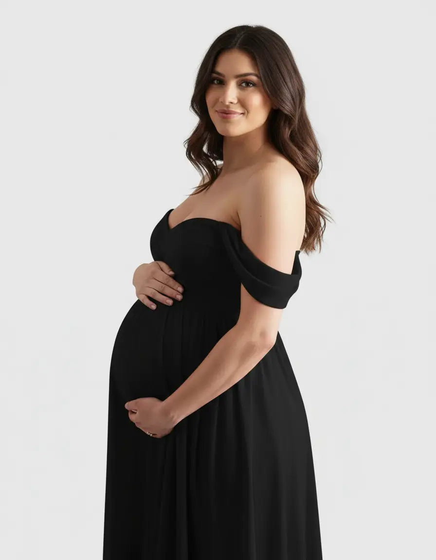 Pregnant woman in a black off-shoulder flowing maternity photoshoot gown, cradling her baby bump.