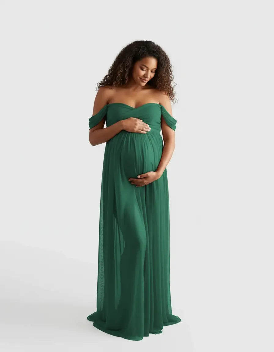 Pregnant woman in a flowing, off-shoulder emerald green maternity photoshoot gown, cradling her bump.