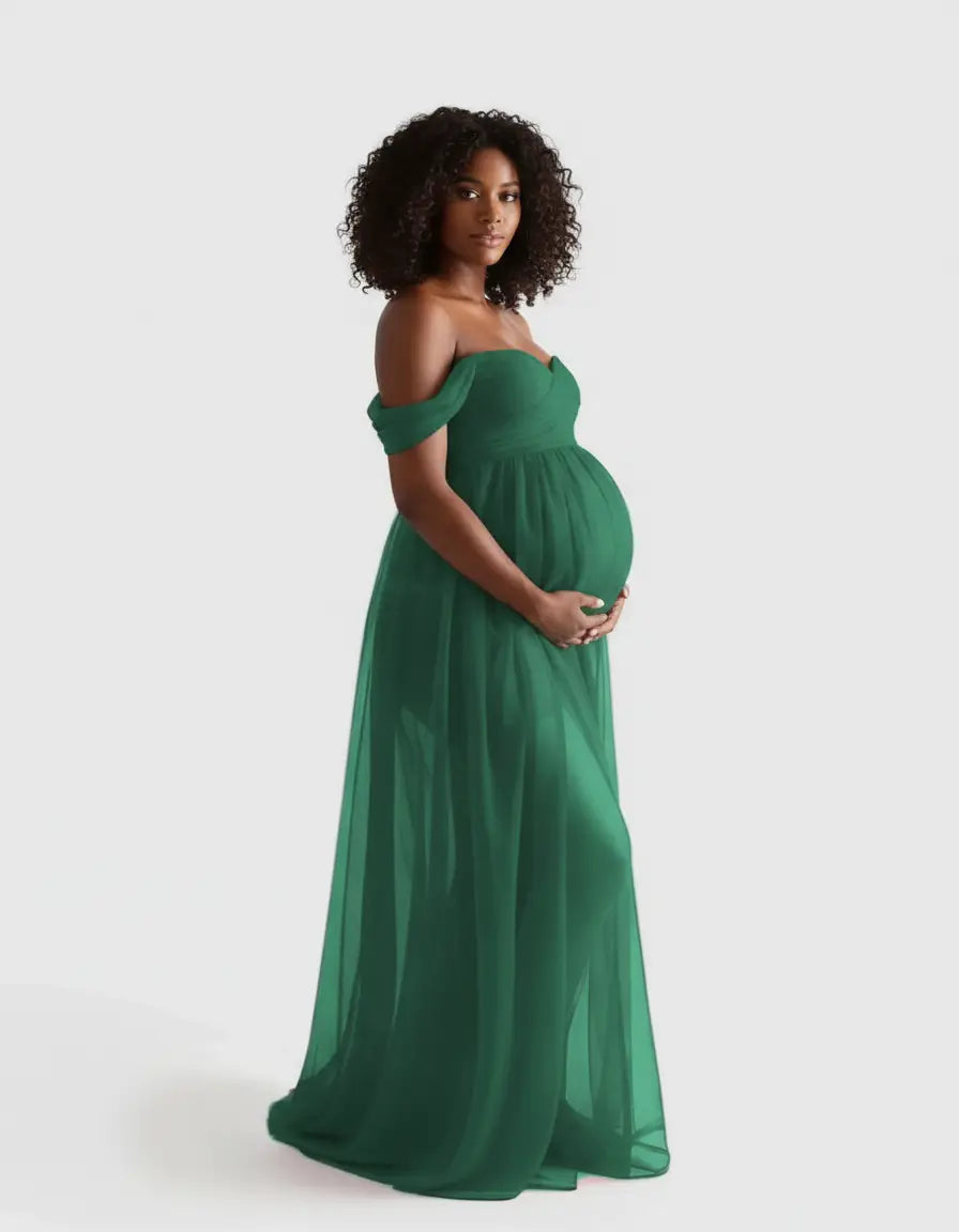 Pregnant woman in a flowing, off-shoulder emerald green maternity photoshoot gown.