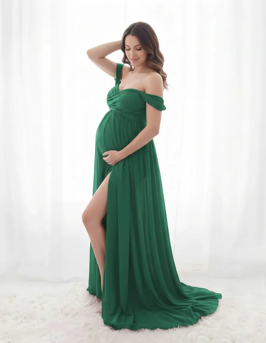 Pregnant woman in a flowing, off-shoulder emerald green maternity gown with a thigh-high slit.