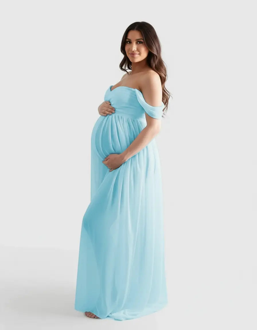 Pregnant woman in a flowing, light blue off-shoulder maternity photoshoot gown, cradling her belly.
