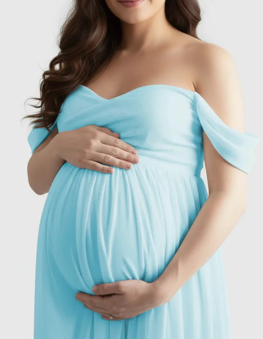 Pregnant woman in a flowing, light blue off-shoulder maternity photoshoot gown, cradling her baby bump.