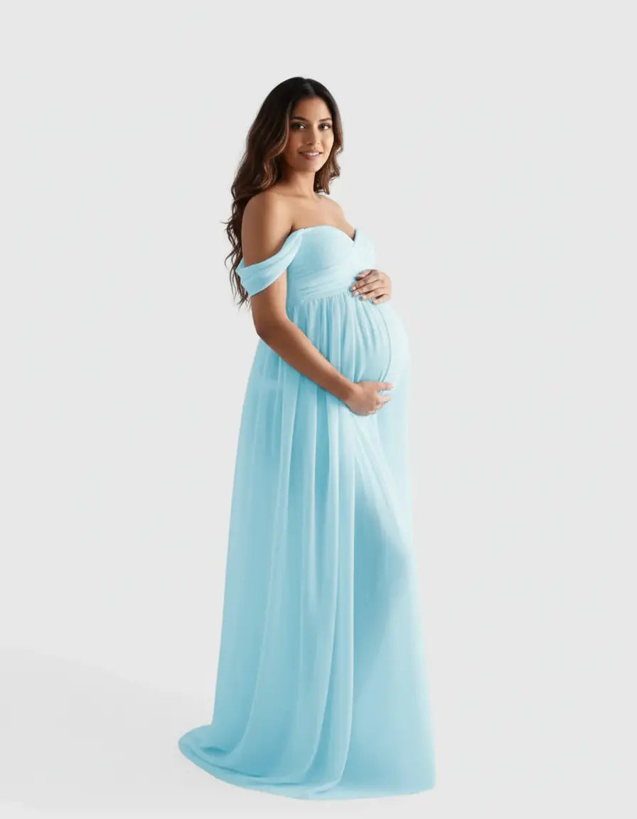 Smiling pregnant woman in a flowing, light blue off-shoulder maternity photoshoot gown.