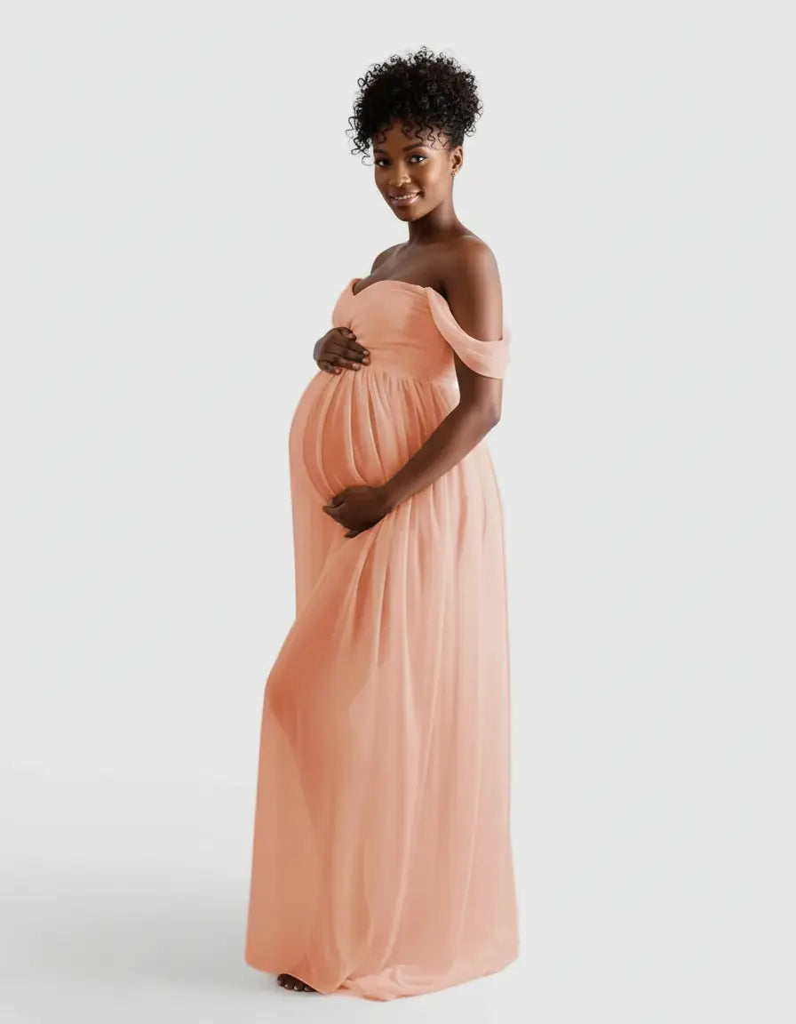 Smiling pregnant woman in a flowing peach off-shoulder maternity photoshoot gown.