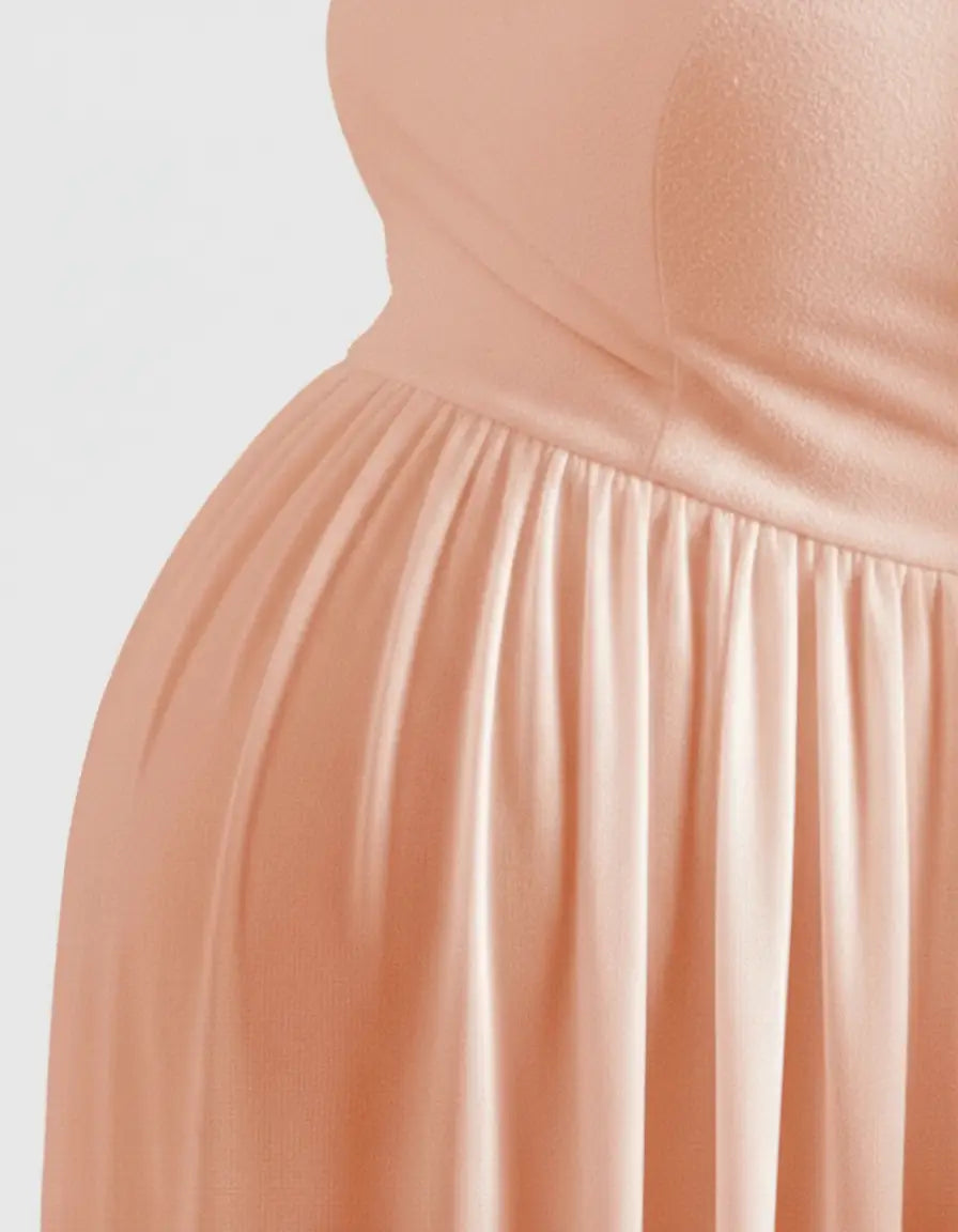 Close-up of a pregnant belly in a flowing, peach off-shoulder maternity photoshoot gown.