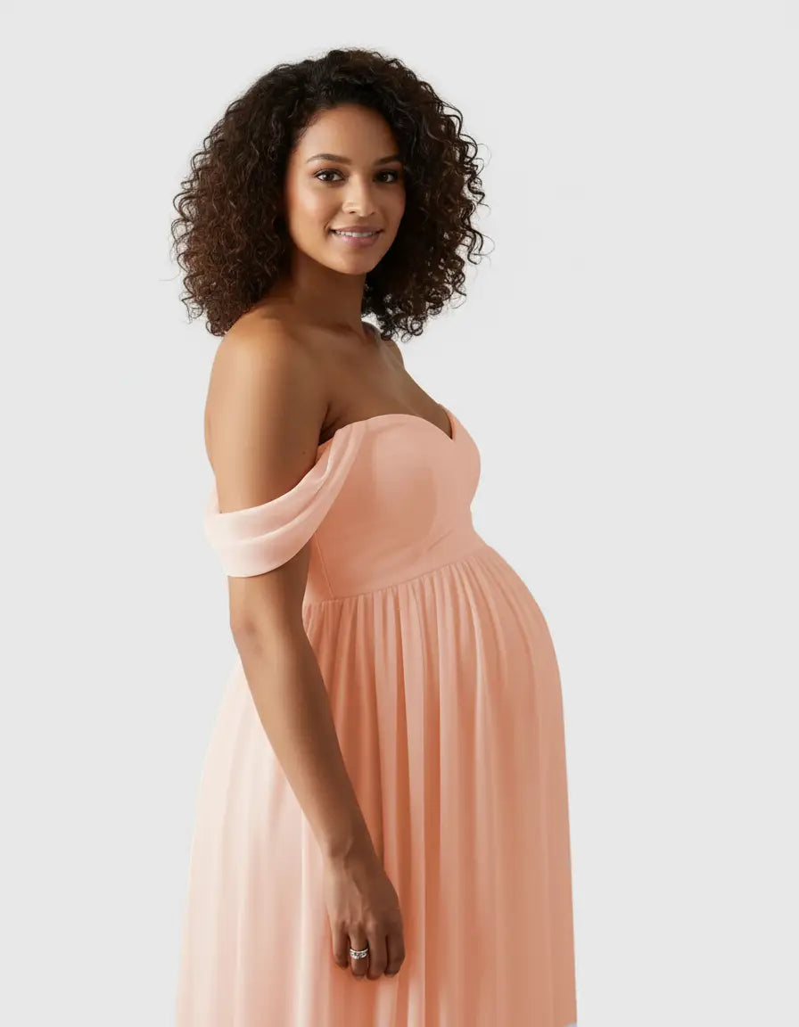 Smiling pregnant woman in a flowing, off-shoulder peach maternity photoshoot gown.
