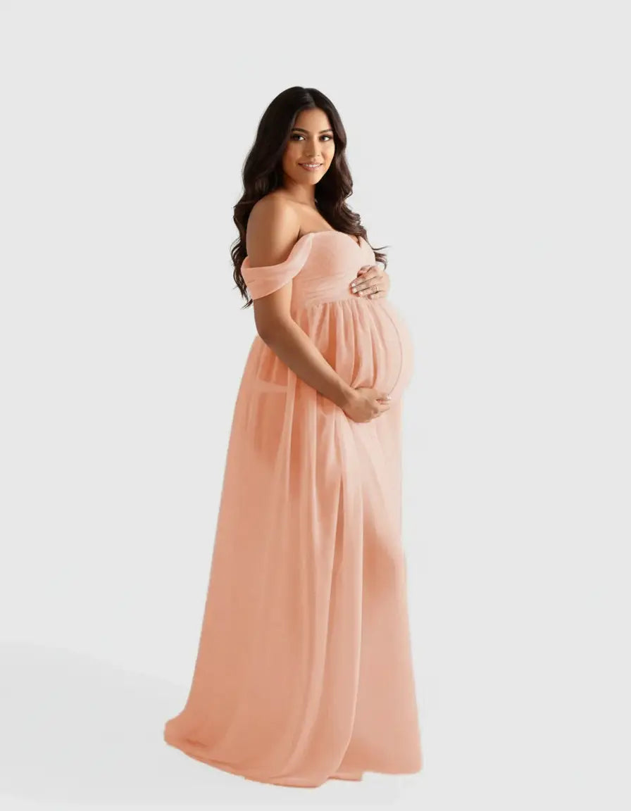 Smiling pregnant woman in a flowing, peach off-shoulder maternity photoshoot gown.