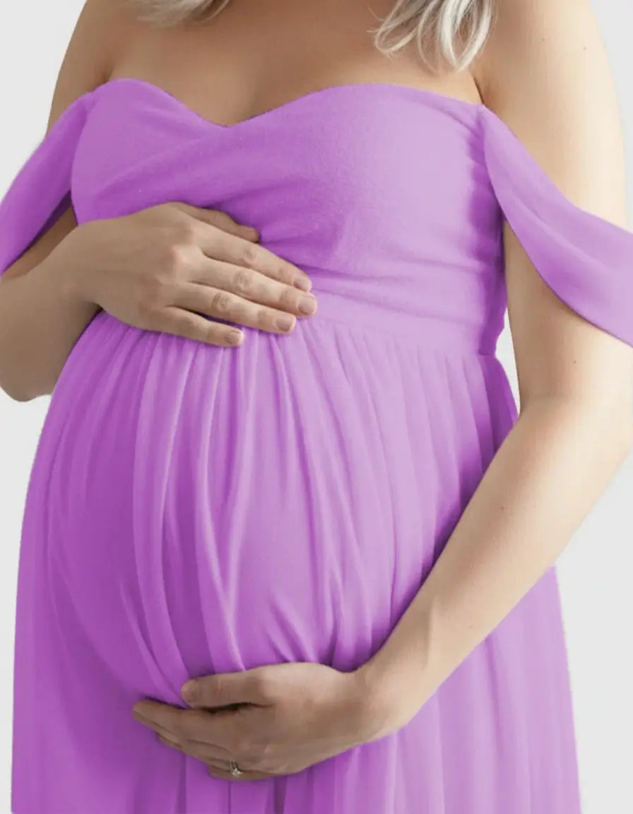 Pregnant woman in a flowing, off-shoulder lavender maternity photoshoot gown, hands cradling her belly.