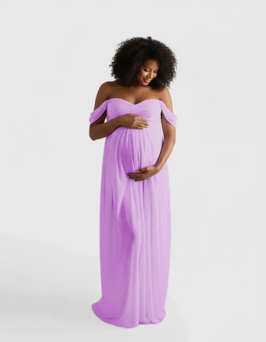 Smiling pregnant woman in a flowing, off-shoulder lavender maternity photoshoot gown.