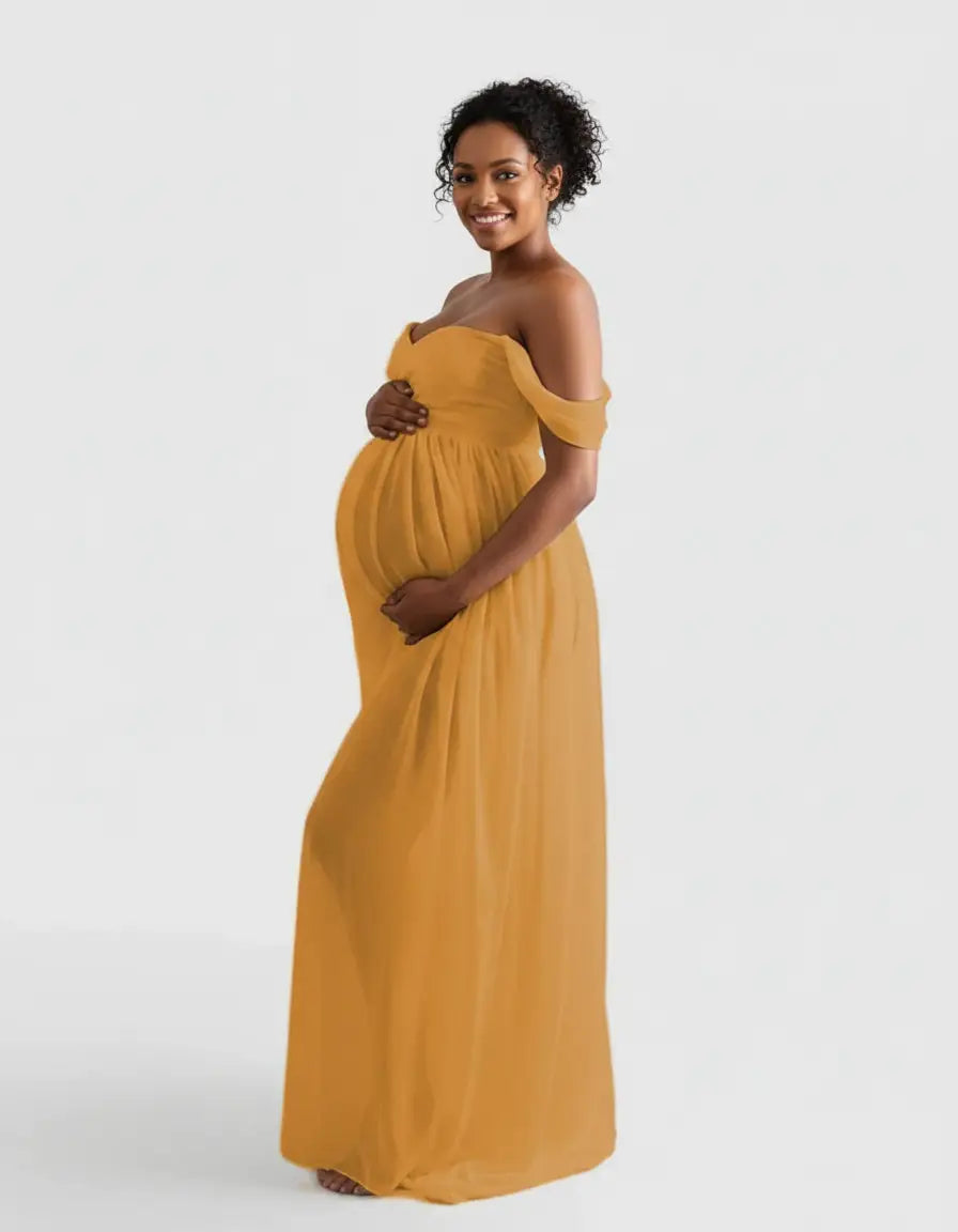 Smiling pregnant woman in a flowing, off-shoulder mustard yellow maternity photoshoot gown.