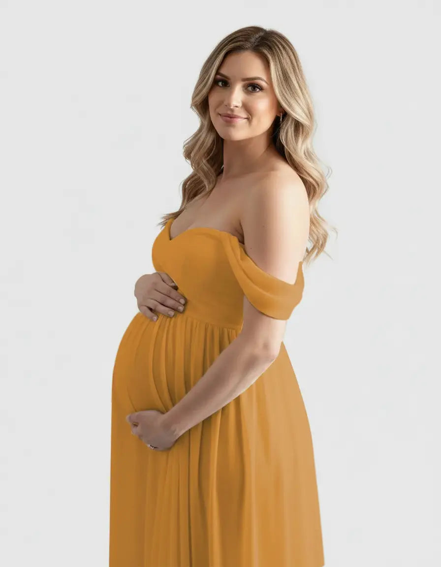 Pregnant woman in a flowing, off-shoulder mustard yellow maternity photoshoot gown, cradling her bump.