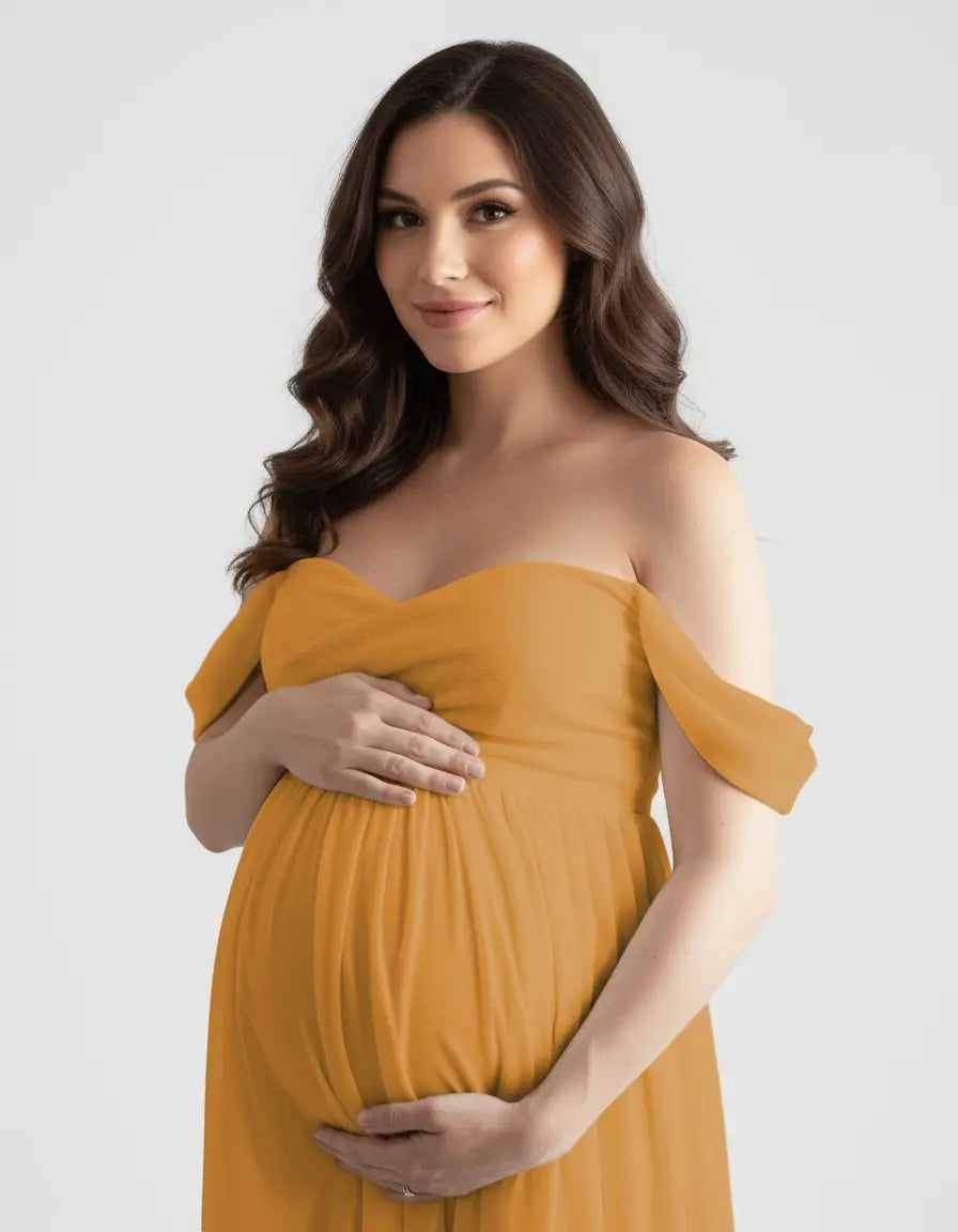 Pregnant woman in a flowing, off-shoulder mustard yellow maternity photoshoot gown, cradling her bump.