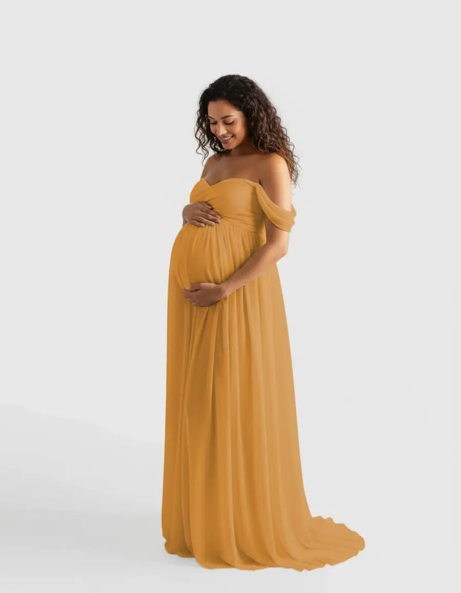 Smiling pregnant woman in a flowing, off-shoulder mustard yellow maternity photoshoot gown.