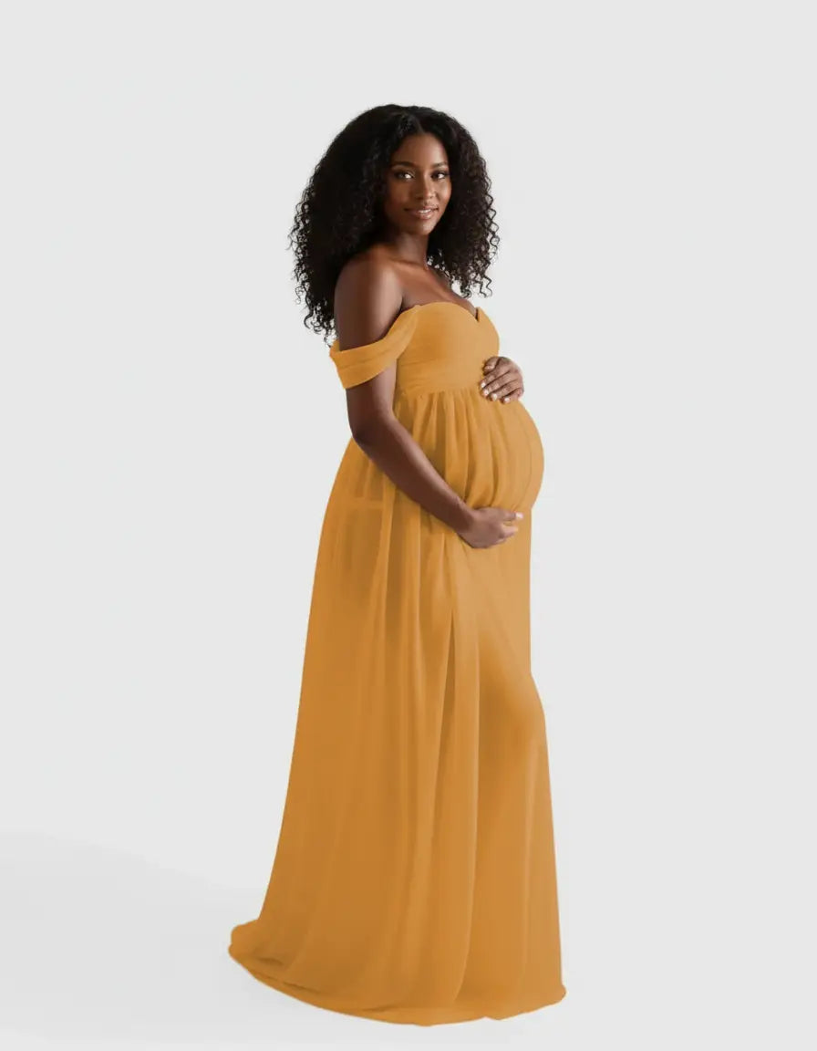 Smiling pregnant woman in a flowing, off-shoulder mustard yellow maternity photoshoot gown.