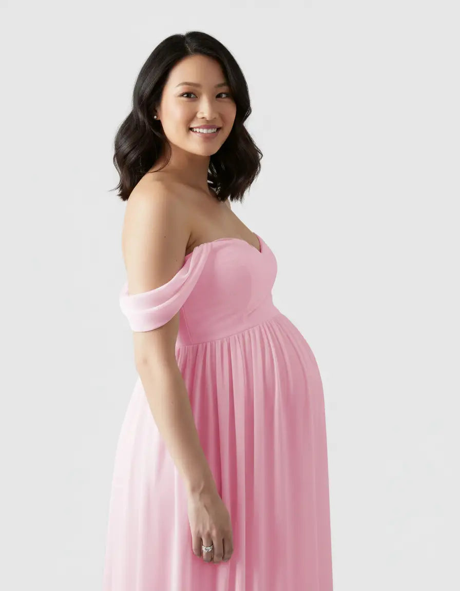 Smiling pregnant woman in a flowing, off-shoulder pink maternity photoshoot gown.