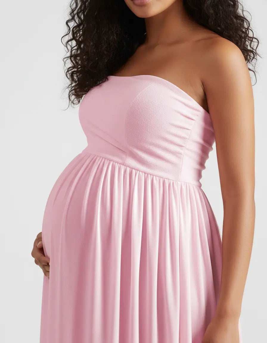 Pregnant woman in a pink off-shoulder flowing maternity gown, hand on baby bump.