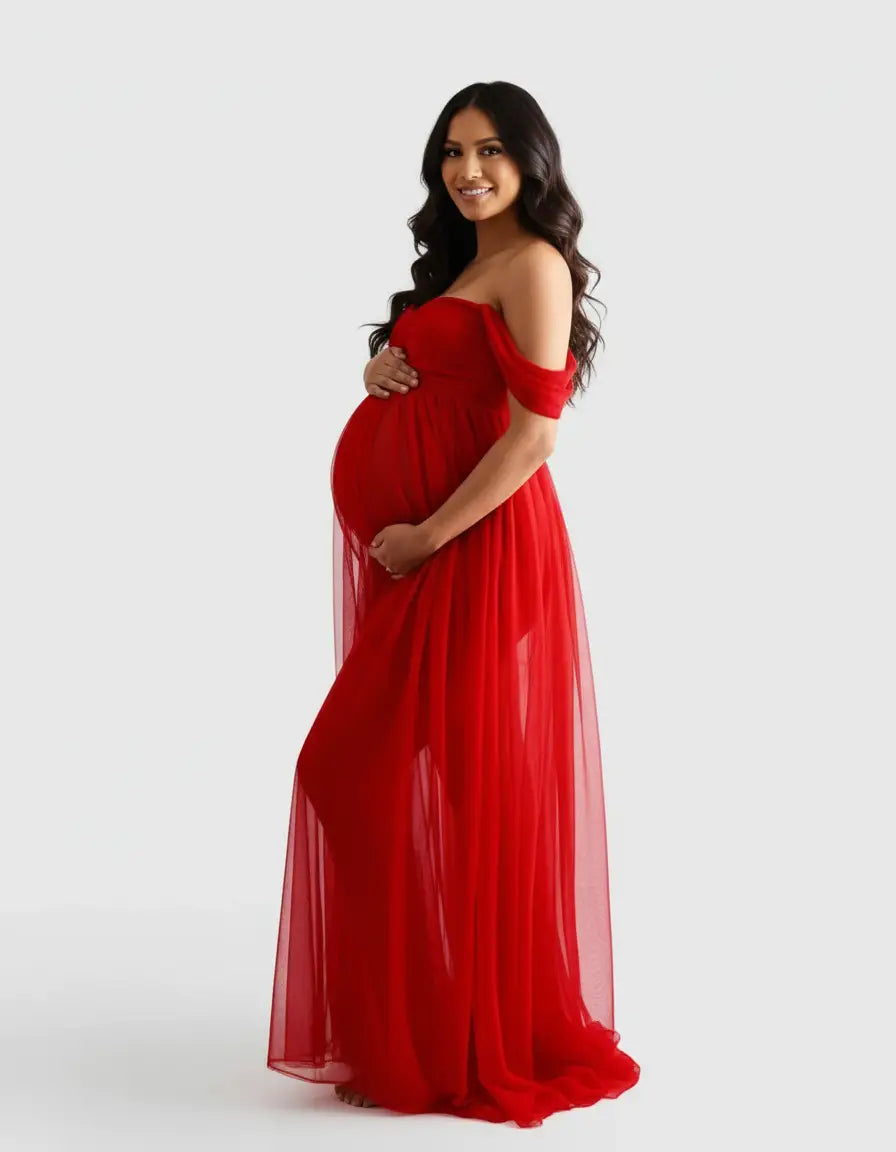 Smiling pregnant woman in a flowing, sheer red off-shoulder maternity photoshoot gown.