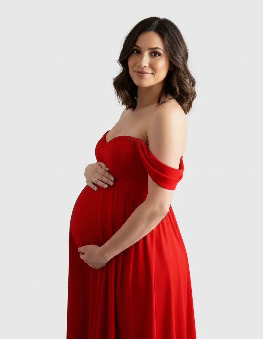 Pregnant woman in a flowing red off-shoulder maternity photoshoot gown, cradling her baby bump.