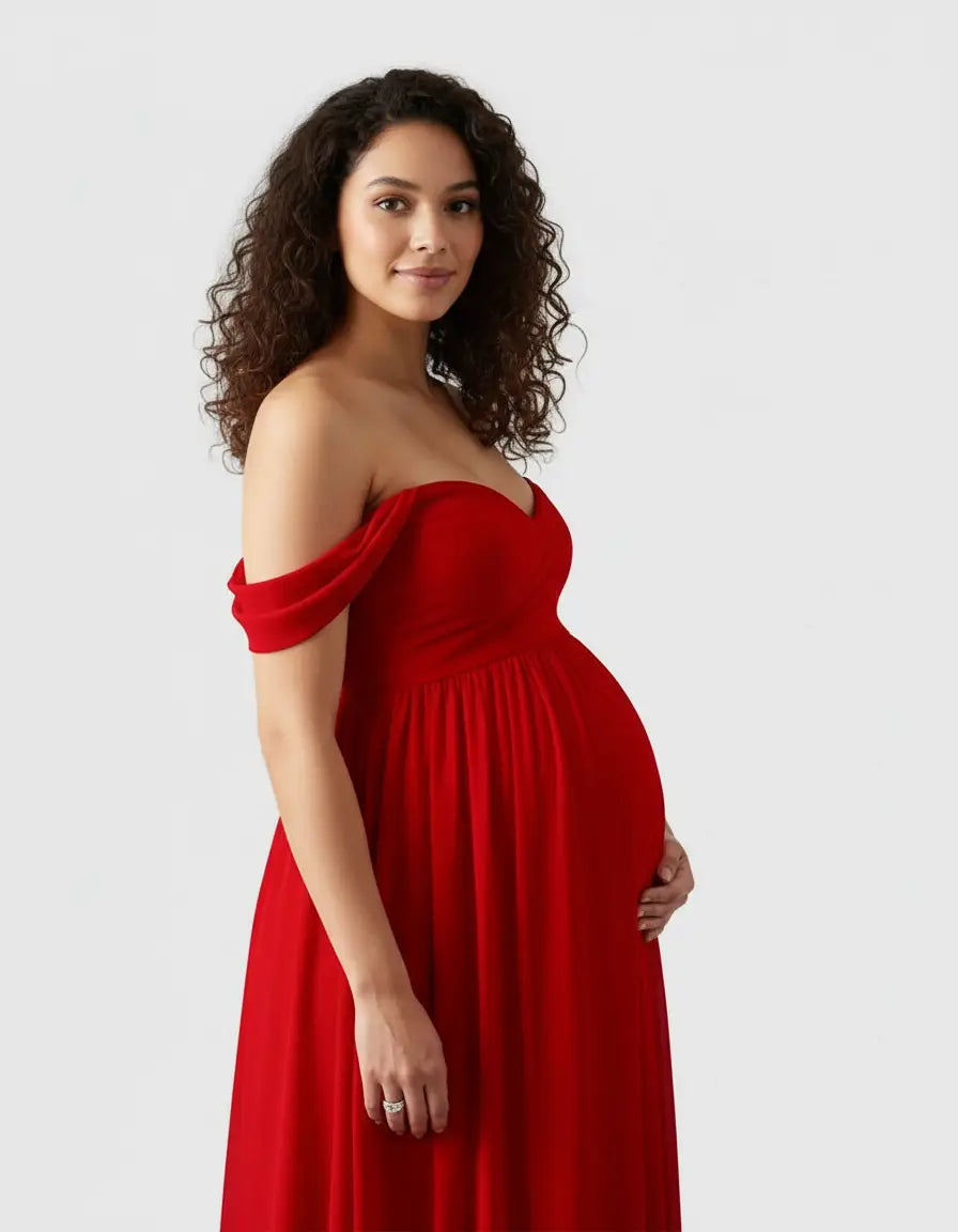 Pregnant woman in a flowing red off-shoulder maternity photoshoot gown, gently holding her bump.