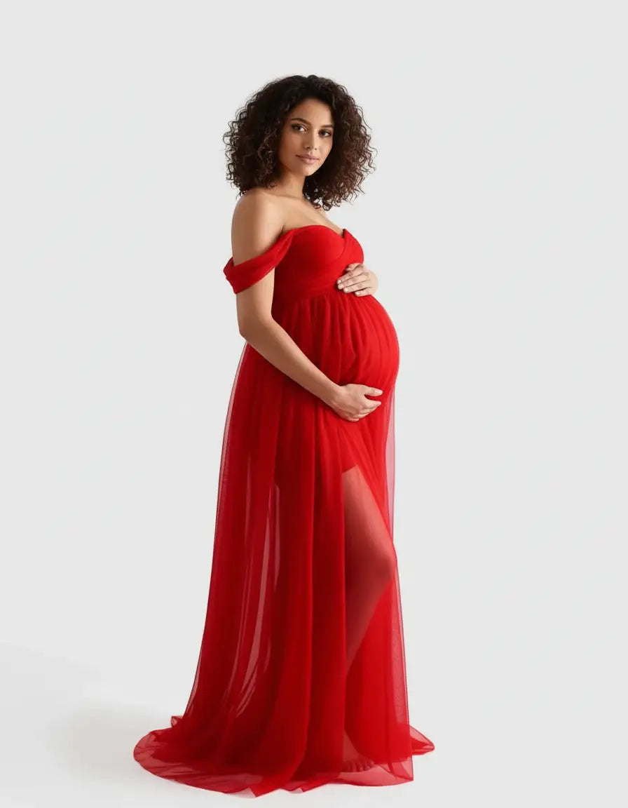 Pregnant woman in a flowing red off-shoulder maternity photoshoot gown with a thigh-high slit.