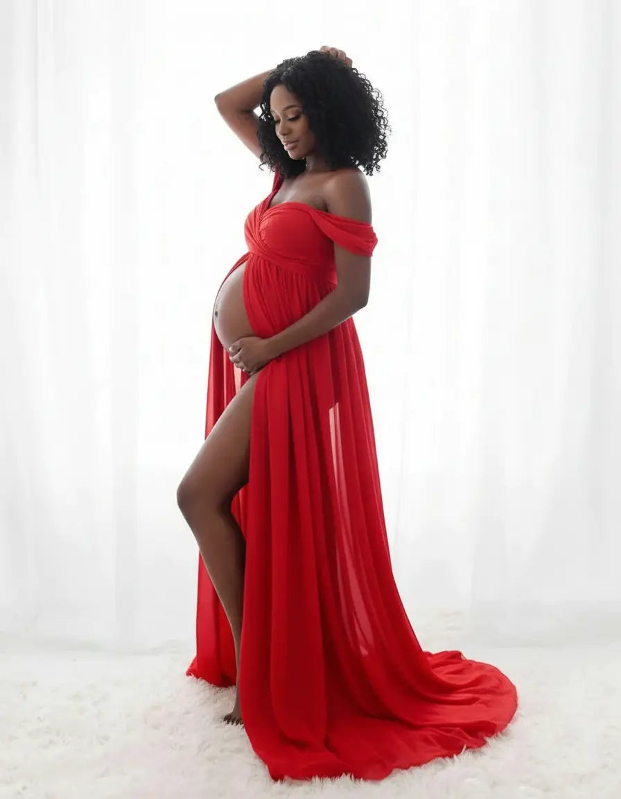 Pregnant woman in a flowing red off-shoulder maternity photoshoot gown with a high slit.