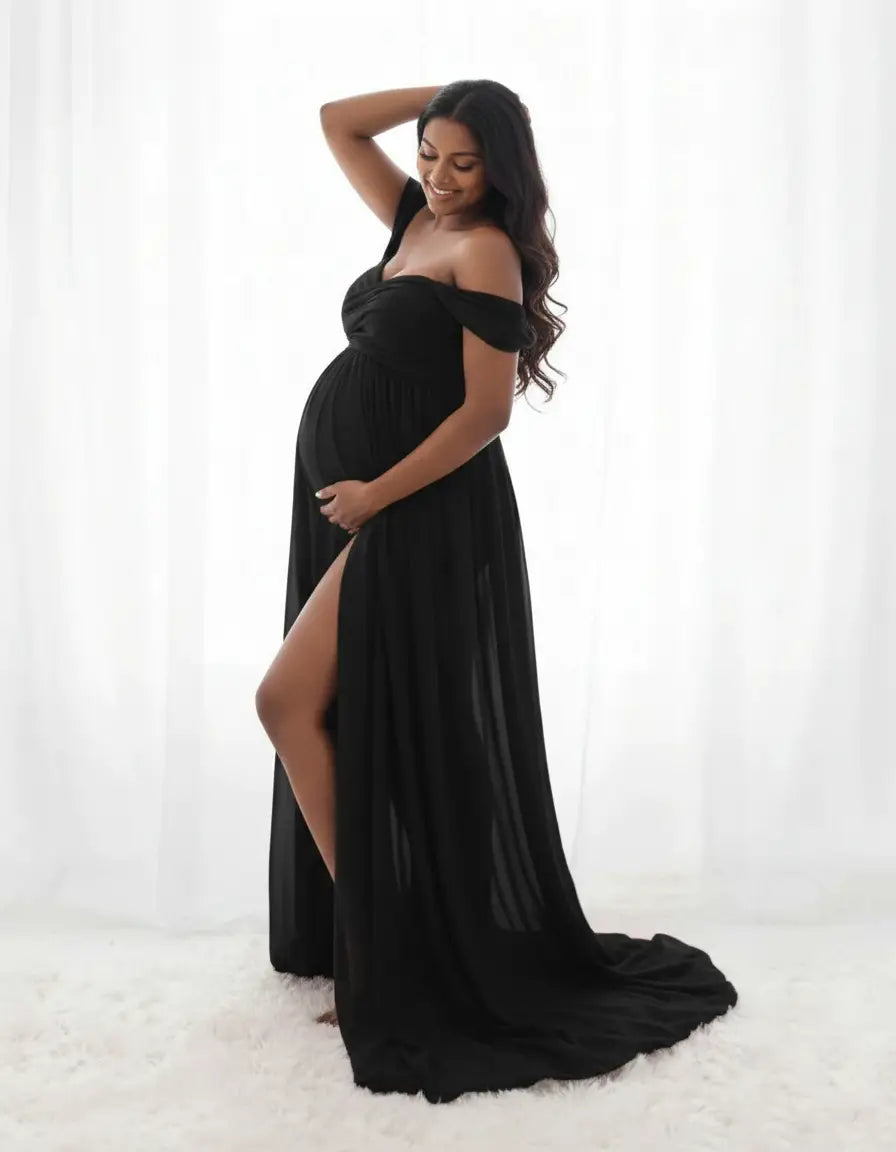Smiling pregnant woman in a black off-shoulder flowing maternity photoshoot gown with a thigh-high slit.