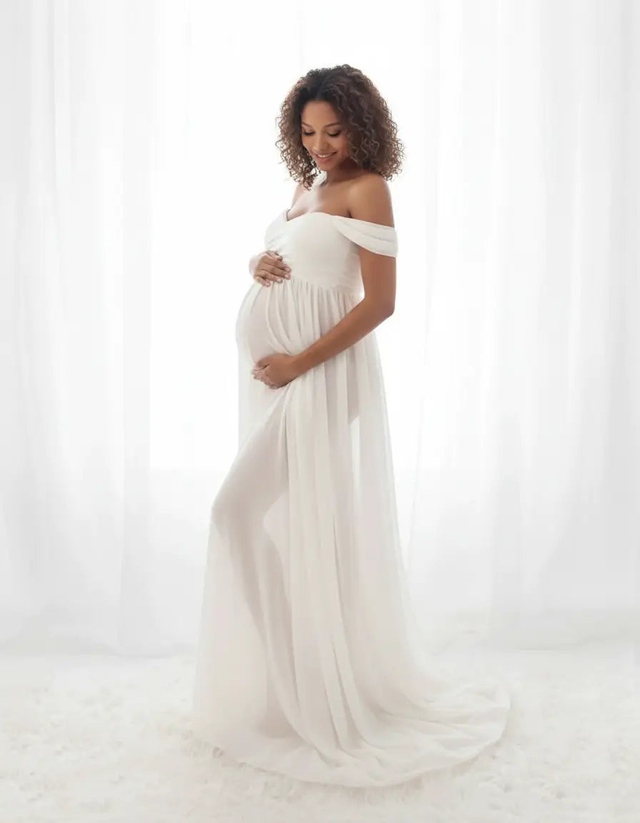Smiling pregnant woman in a white off-shoulder flowing maternity photoshoot gown.