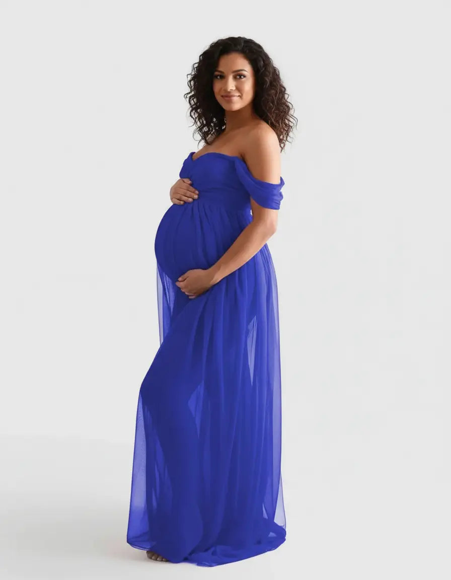 Pregnant woman in a flowing royal blue off-shoulder maternity photoshoot gown, holding her baby bump.