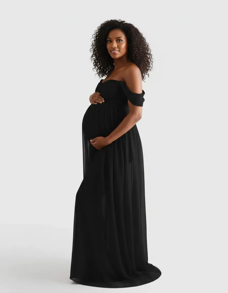 Pregnant woman in a black off-shoulder flowing maternity photoshoot gown, cradling her baby bump.