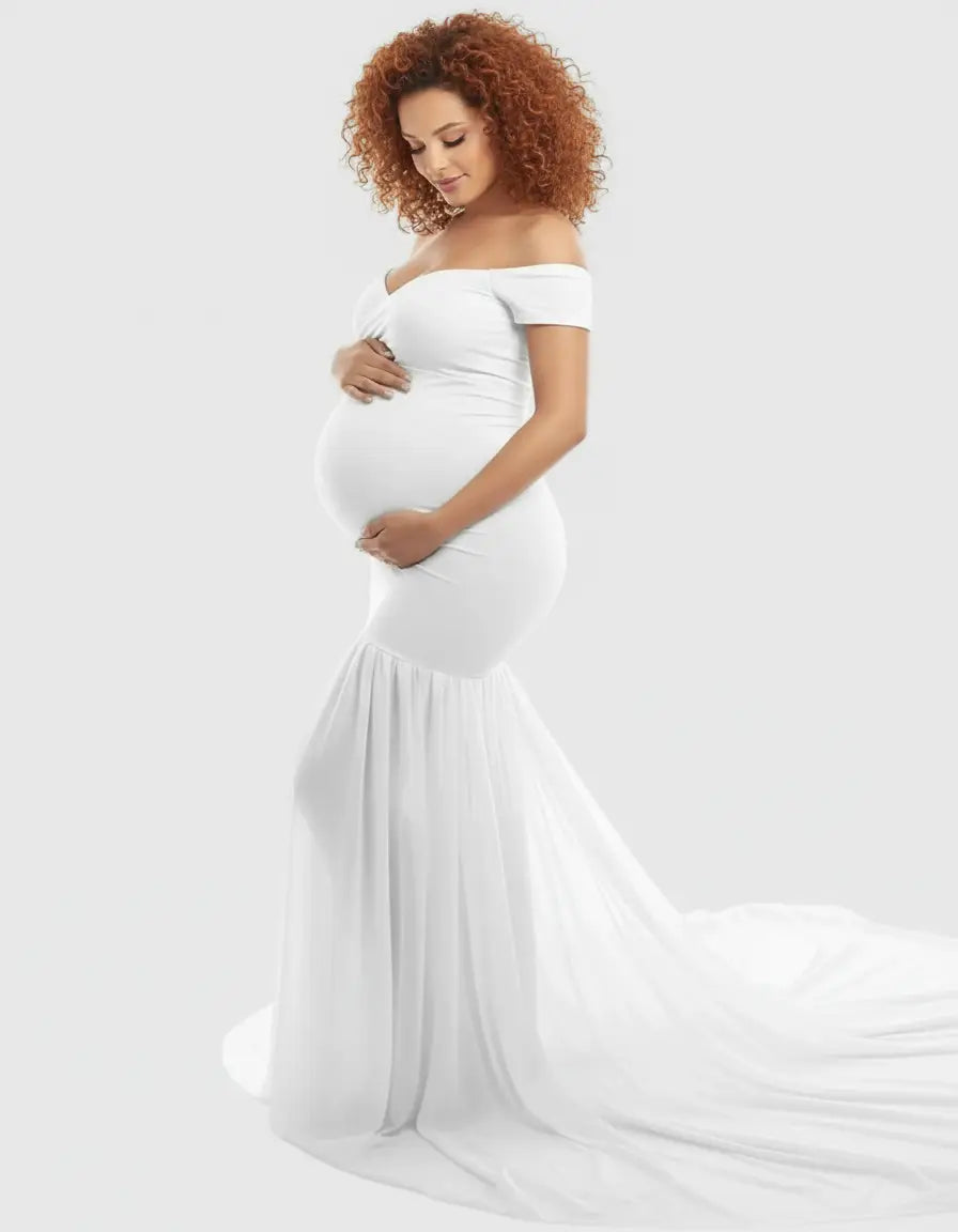 Pregnant woman in a white off-shoulder flowy maternity gown with a long train.
