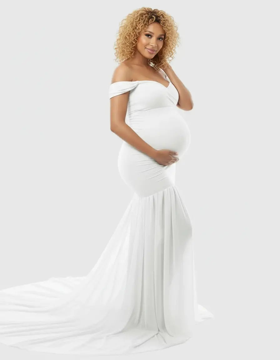 Pregnant woman in a white off-shoulder flowy maternity gown with a long train.
