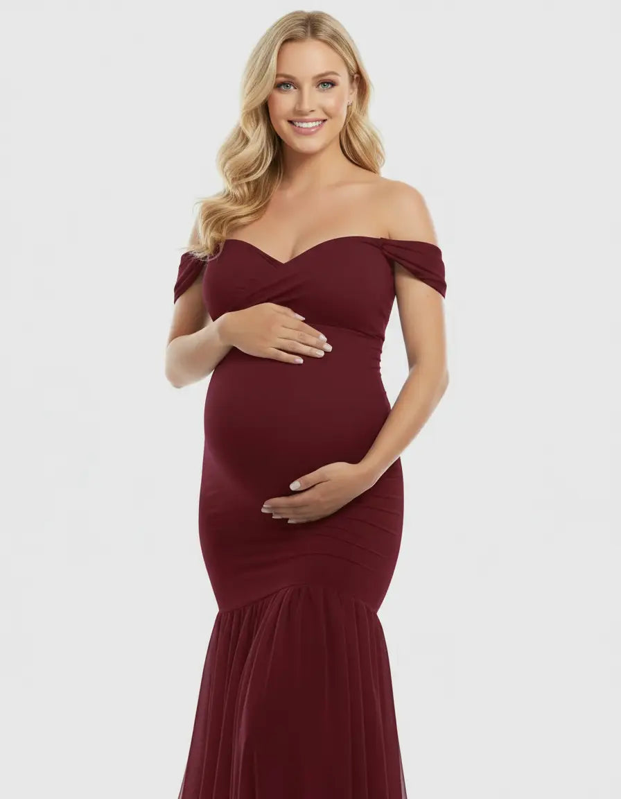 Smiling pregnant woman in a burgundy off-shoulder flowy maternity gown with a mermaid hem.