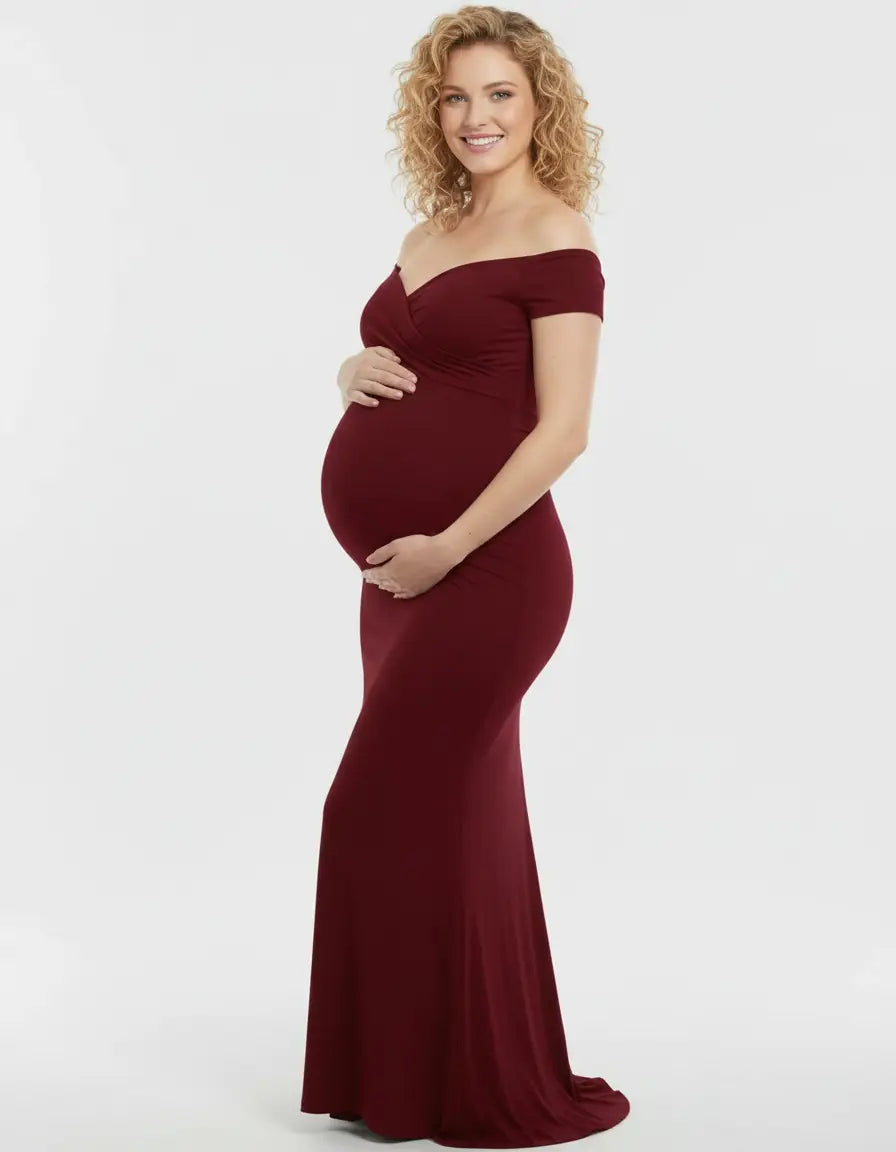 Smiling pregnant woman in a flowy, off-shoulder burgundy maternity gown.