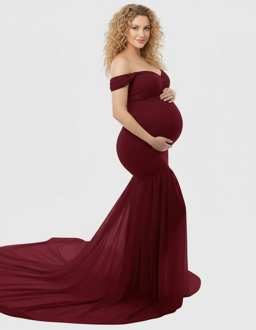 Pregnant woman in a flowy, off-shoulder, deep red maternity gown with a long train.
