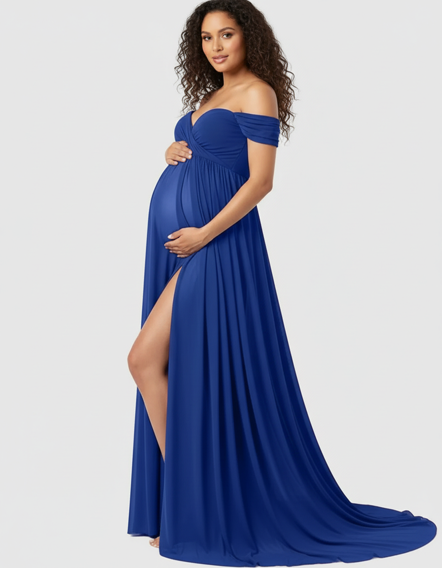Maternity model in a flowing royal blue off-shoulder maxi dress with a thigh-high slit, cradling her baby bump.